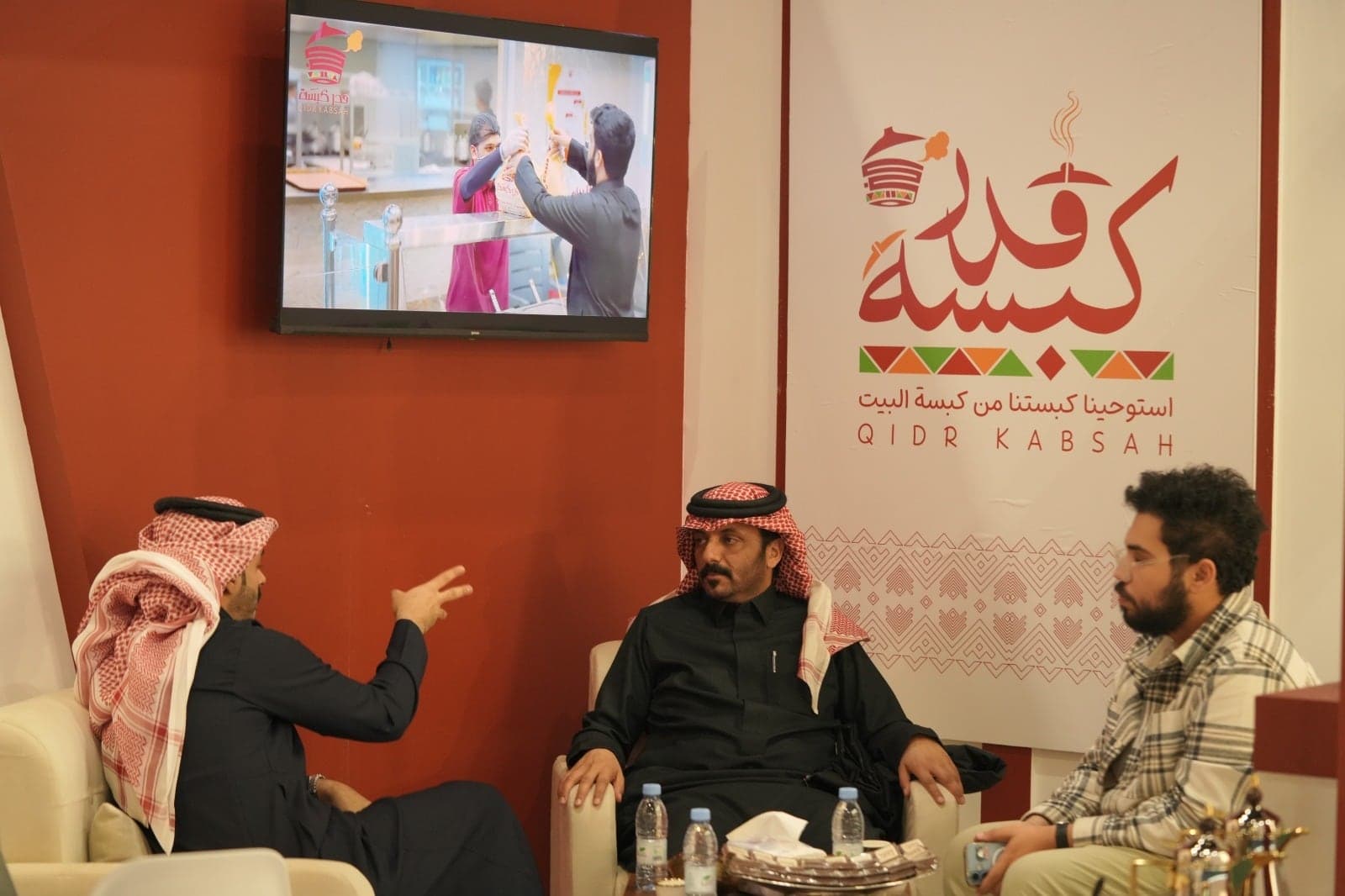 ثلاثة أطراف يجلسون في نقاش عند جناح امتياز سعودي للأغذية