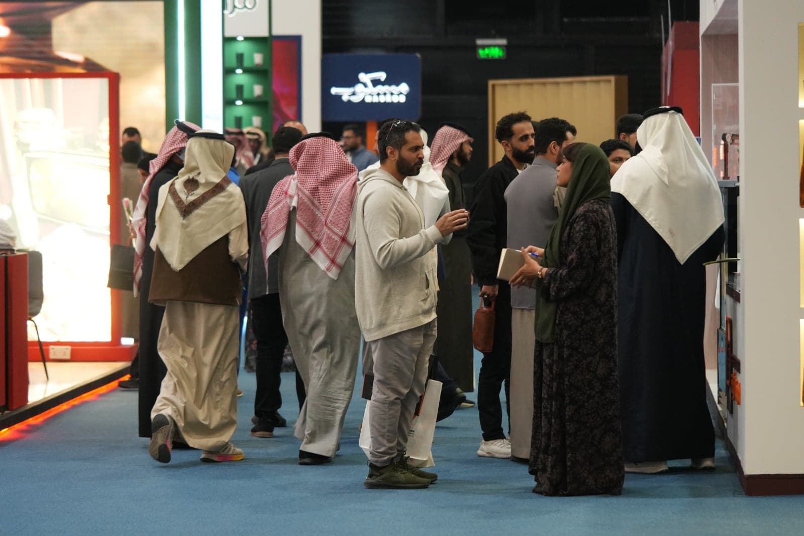 زوار يسيرون في ممر المعرض بمحاذاة أجنحة مضاءة للعلامات